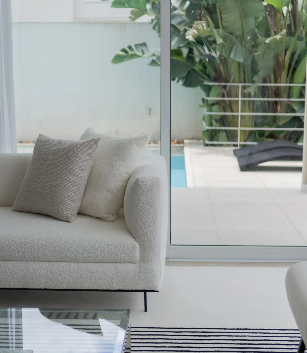 Sunlit luxury living room with a cream sofa and a view of the pool and palms through glass doors